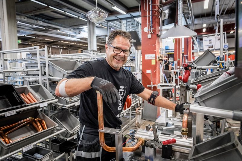A man working with copper pipes in an industrial environment at Bosch Thermoteknik. He is wearing work clothes and safety glasses, and looks happy while performing his task. Binar Solutions helped Bosch Thermoteknik achieve increased efficiency through Takt and Andon.