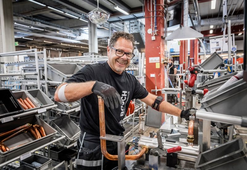 A man working with copper pipes in an industrial environment at Bosch Thermoteknik. He is wearing work clothes and safety glasses, and looks happy while performing his task. Binar Solutions helped Bosch Thermoteknik achieve increased efficiency through Takt and Andon.