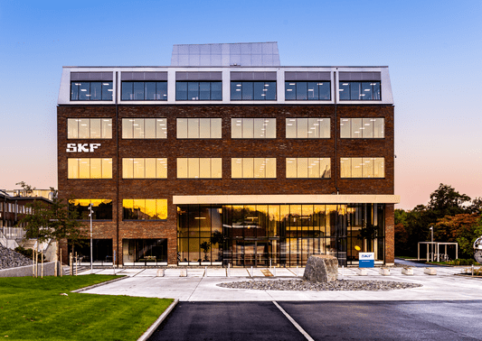 Exterior view of SKF's head office building at sunset, with modern architecture and large windows reflecting the sky. Binar Solution helped sharpen their production processes.